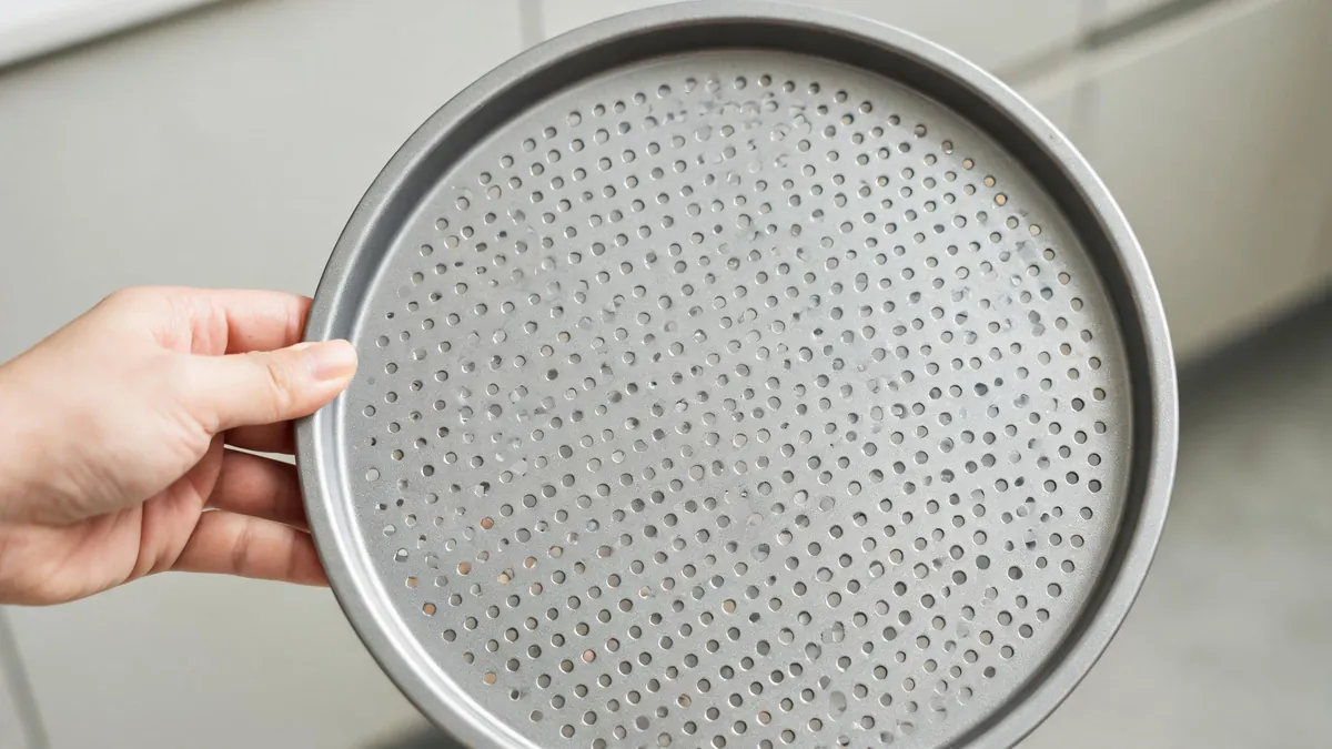 Perforated round air fryer tray beside a compact air fryer on a clean kitchen counter