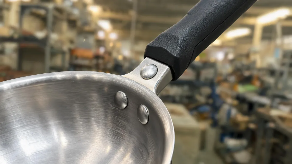 Frying pan with a riveted stainless handle and a glass lid beside a spec sheet on a kitchen counter