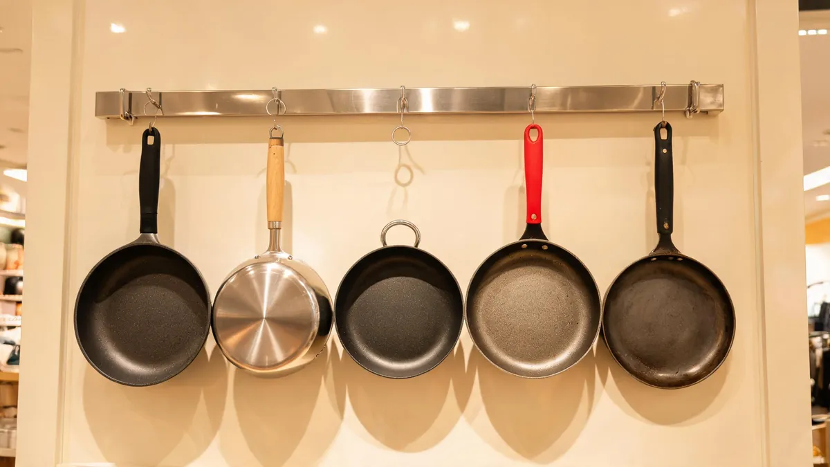 Frying pan with a riveted stainless handle and a glass lid beside a spec sheet on a kitchen counter